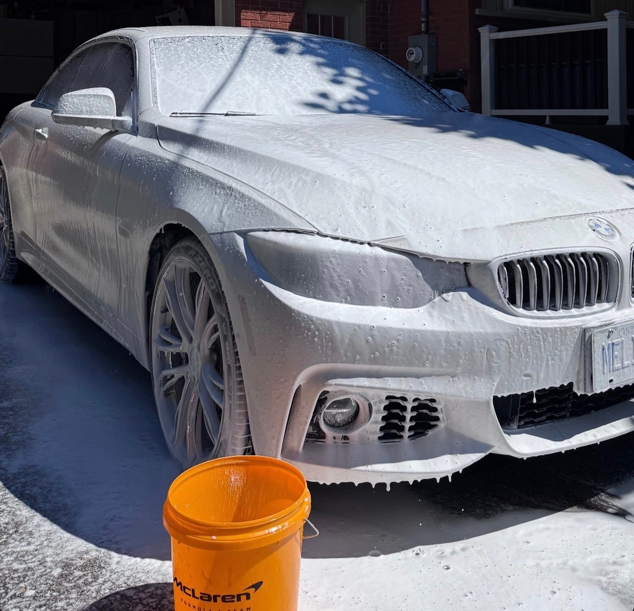 A BMW coupe covered in white snow foam during a hand wash in a driveway